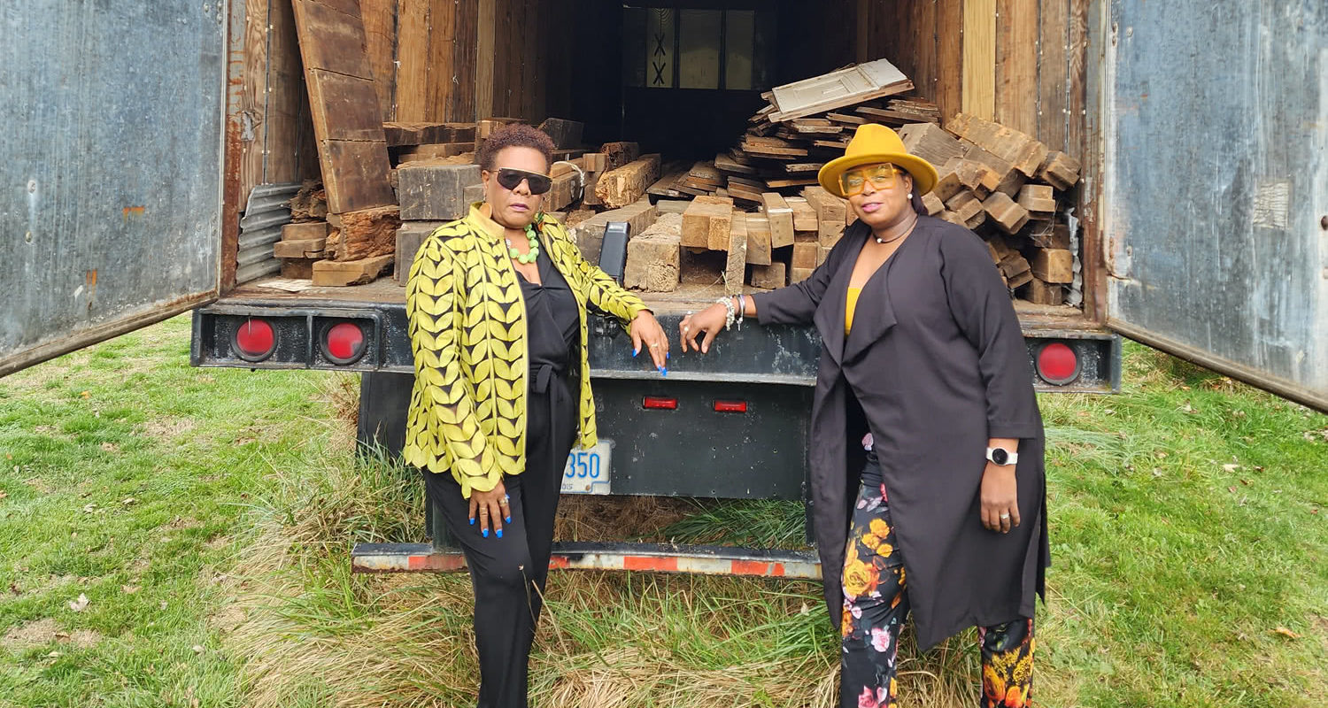 Southampton African American Museum & Eastville Historical Society: Two women are leaning on the edge of an open box truck full of wood planks.