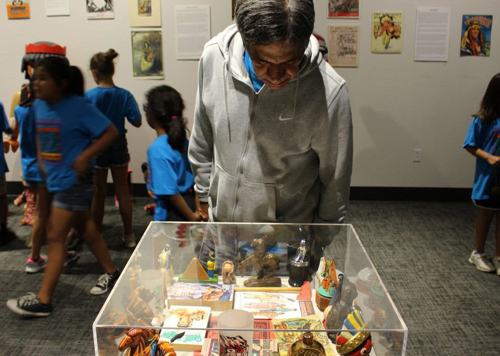 Seneca Museum - A person stands over a glass display, looking down at a part of an exhibit. Behind them are a group of children in matching blue t-shirts - they look like they’re on a school field trip.