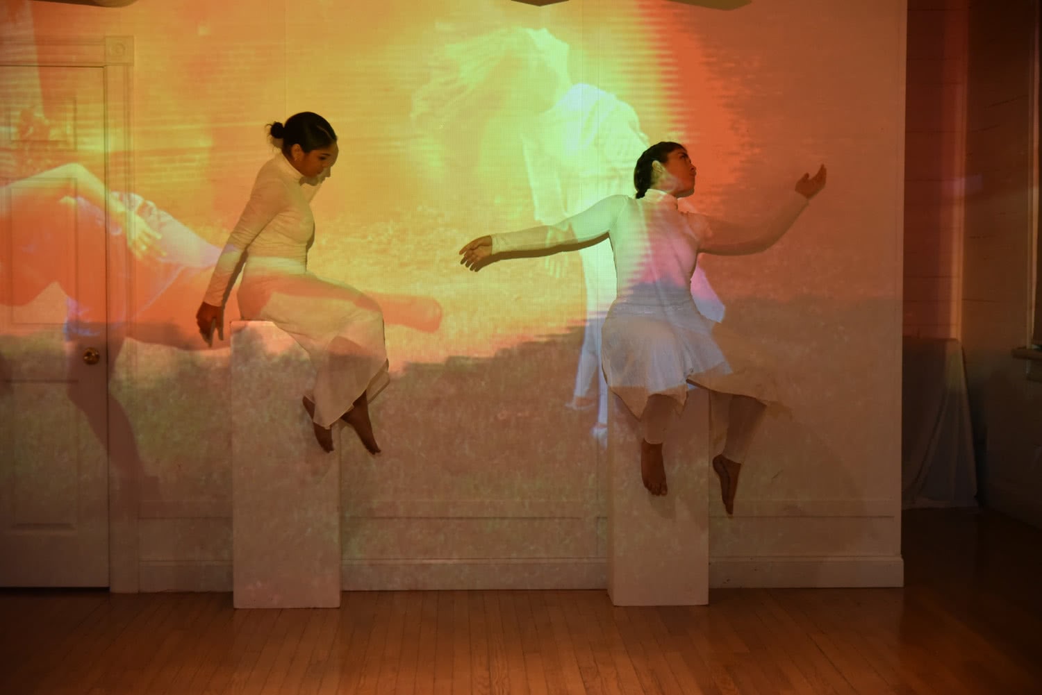Teatro Yerbabruja: Two dancers wearing white flowy costumes are posed on pedestals, as if they were statues in a museum. The two dancers are standing in front of a projection of someone dancing, and because the dancers are wearing white, it’s almost as if the dancers are canvases for the projection themselves.