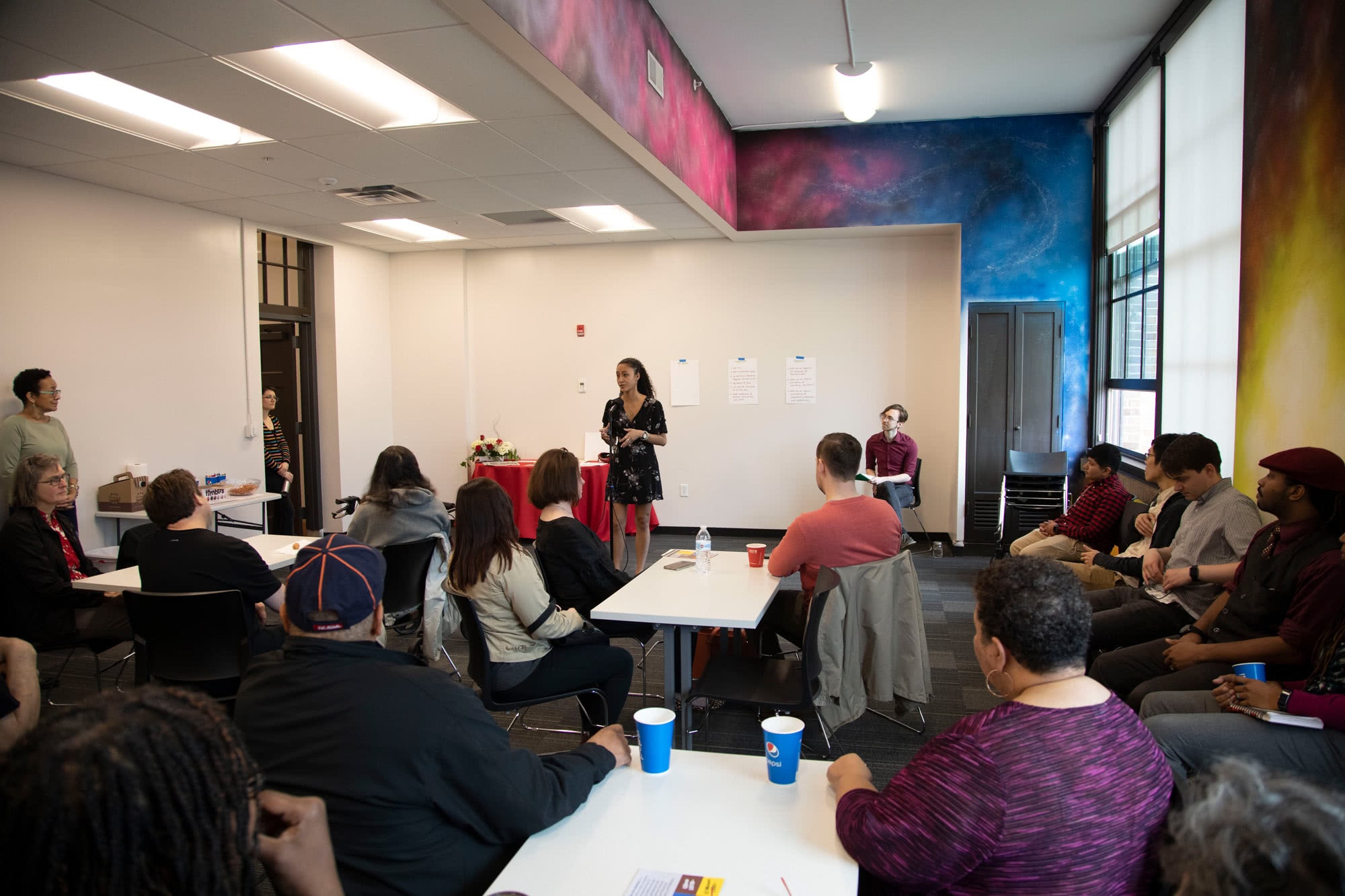 Frontline Arts Buffalo: A person standing in front of a room of people, mid presentation.