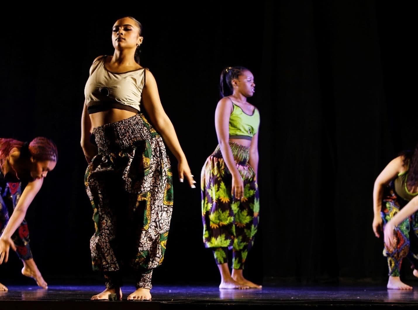 Borinquen Dance Theatre Inc.: Three dancers are on stage in different poses, under dramatic lighting against a black background.