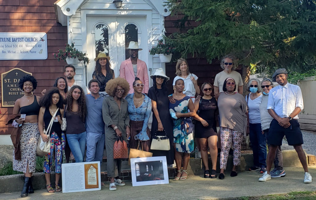 Eastville Historical Society: A group of people are standing in front of a historical site, St. David AME Zion Church - on the ground in front of the crowd are photos of the church interior.