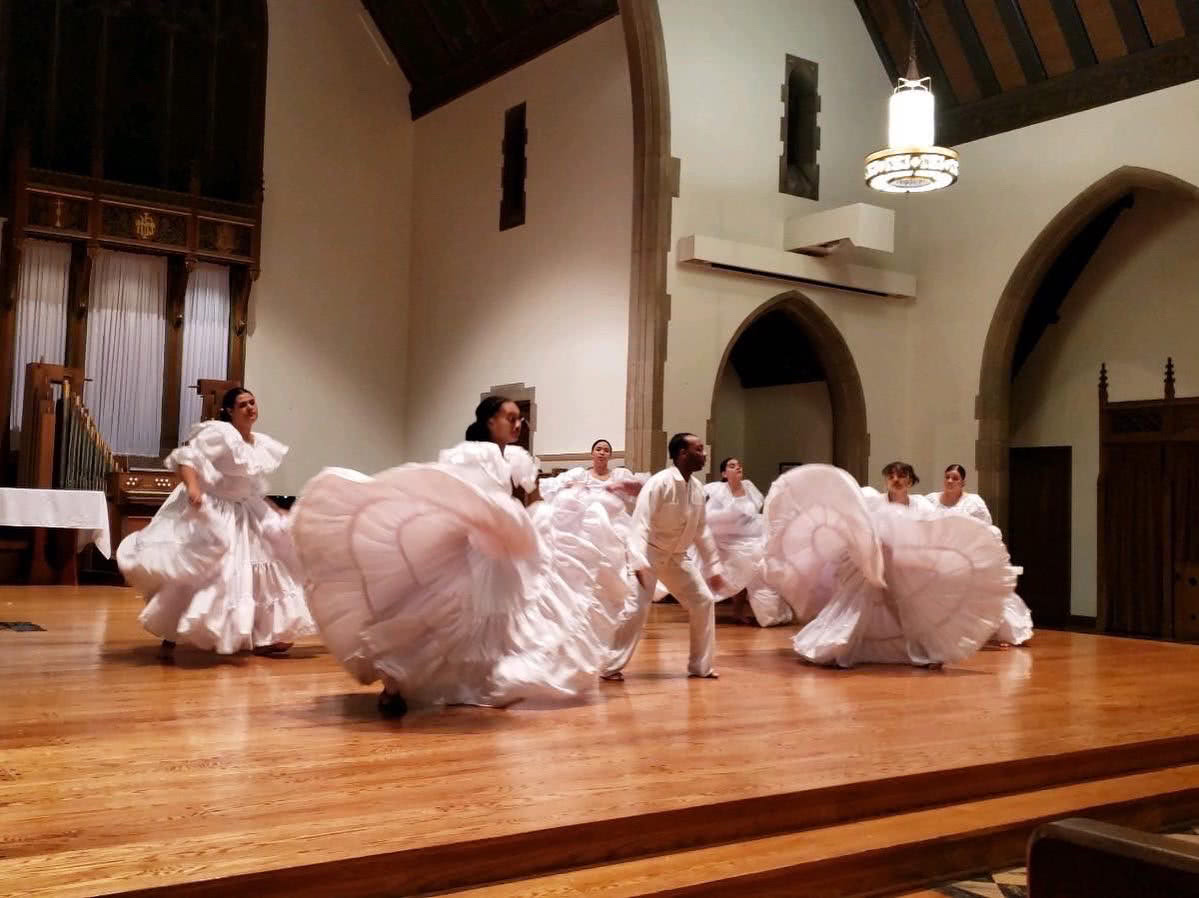 Borinquen Dance Theatre Inc.: A group of dancers wearing all white, ruffled, long dresses on stage. The dancers are twirling and their skirts are flowing up in the air around them.